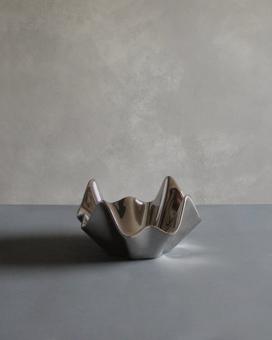 Bowl Platejat de diseño con acabado plateado brillante y forma ondulada sobre fondo gris.